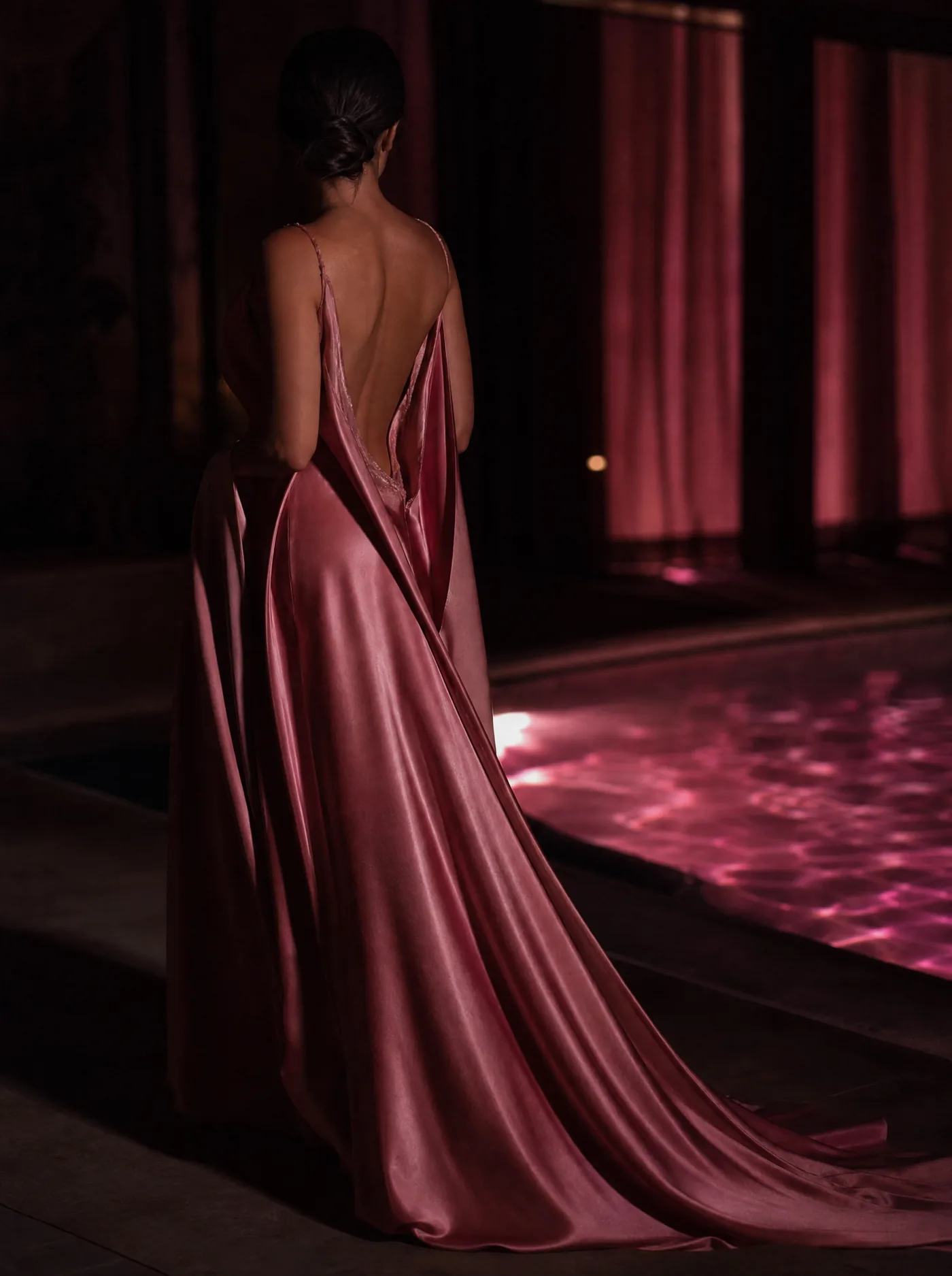 A woman in a flowing blush silk gown beside a softly lit pool